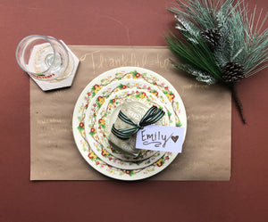 Holiday place setting ideas with fancy plates, wine glass, coaster, holly and pine spring, and an interactive place mat